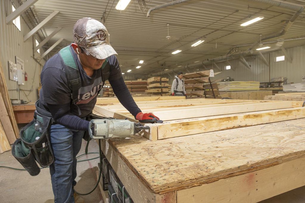 Professional photograph of man using a nail gun on a wooden frame for a wall.