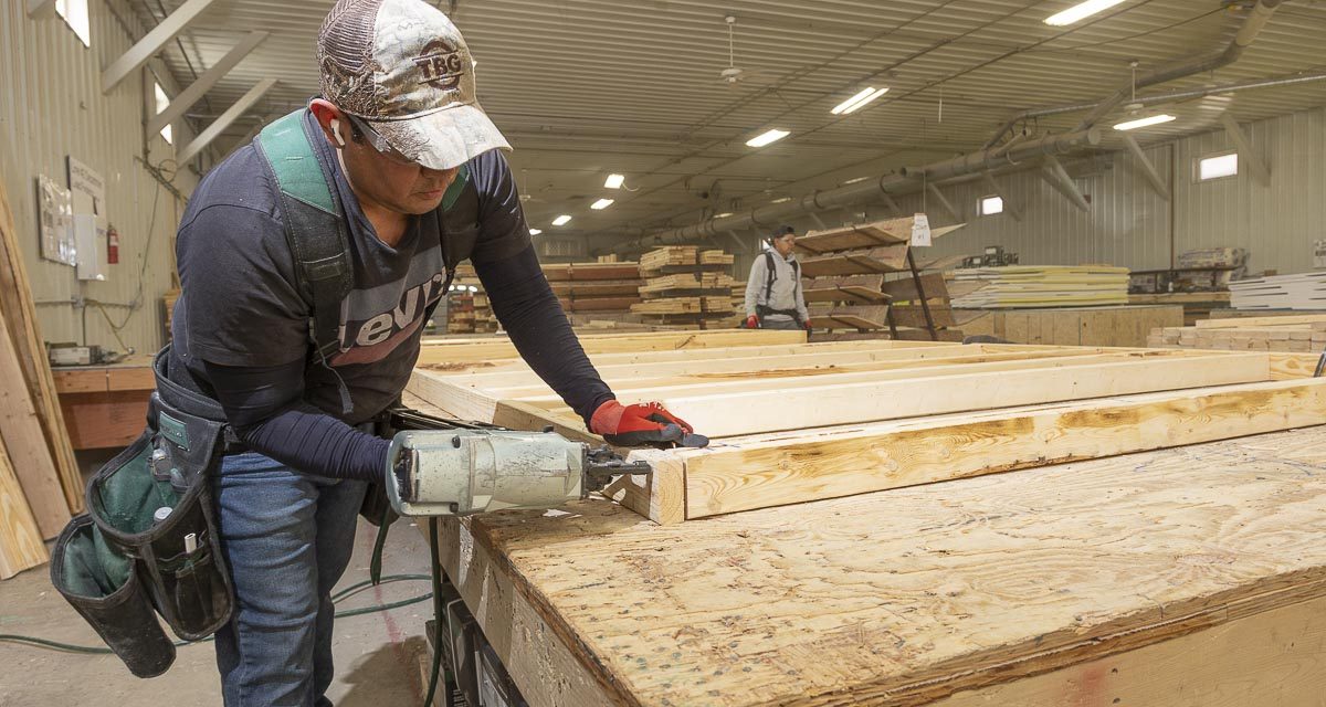 Professional photograph of man using a nail gun on a wooden frame for a wall.
